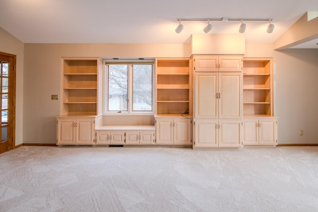 unfurnished living room featuring rail lighting, light carpet, and baseboards