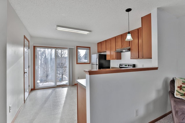 kitchen featuring freestanding refrigerator, under cabinet range hood, pendant lighting, range, and brown cabinets