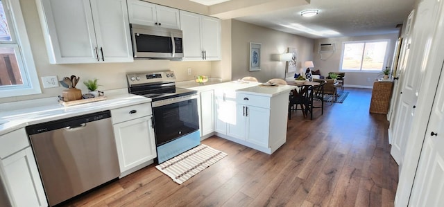 kitchen featuring light wood finished floors, light countertops, appliances with stainless steel finishes, white cabinetry, and a peninsula