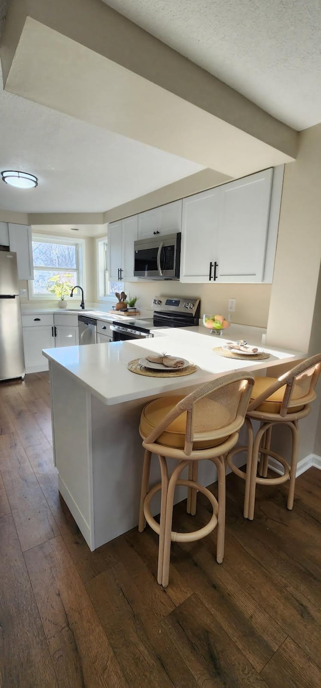 kitchen featuring a peninsula, white cabinetry, appliances with stainless steel finishes, and dark wood finished floors