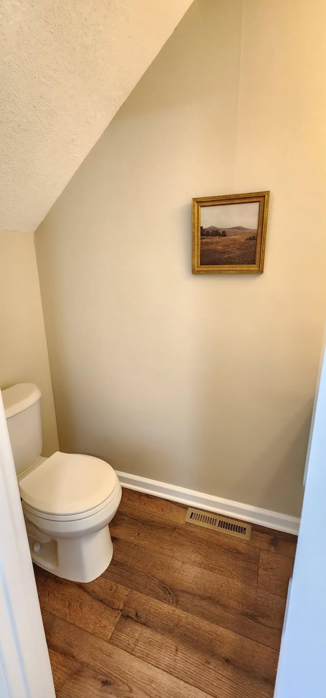 bathroom with baseboards, visible vents, toilet, wood finished floors, and vaulted ceiling