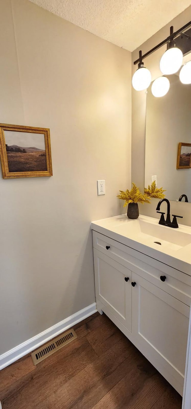 bathroom with a textured ceiling, wood finished floors, vanity, visible vents, and baseboards