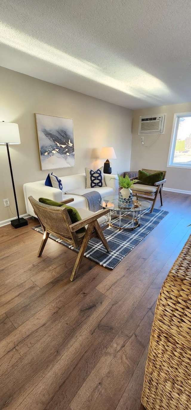 living area with a textured ceiling, hardwood / wood-style floors, a wall unit AC, and baseboards