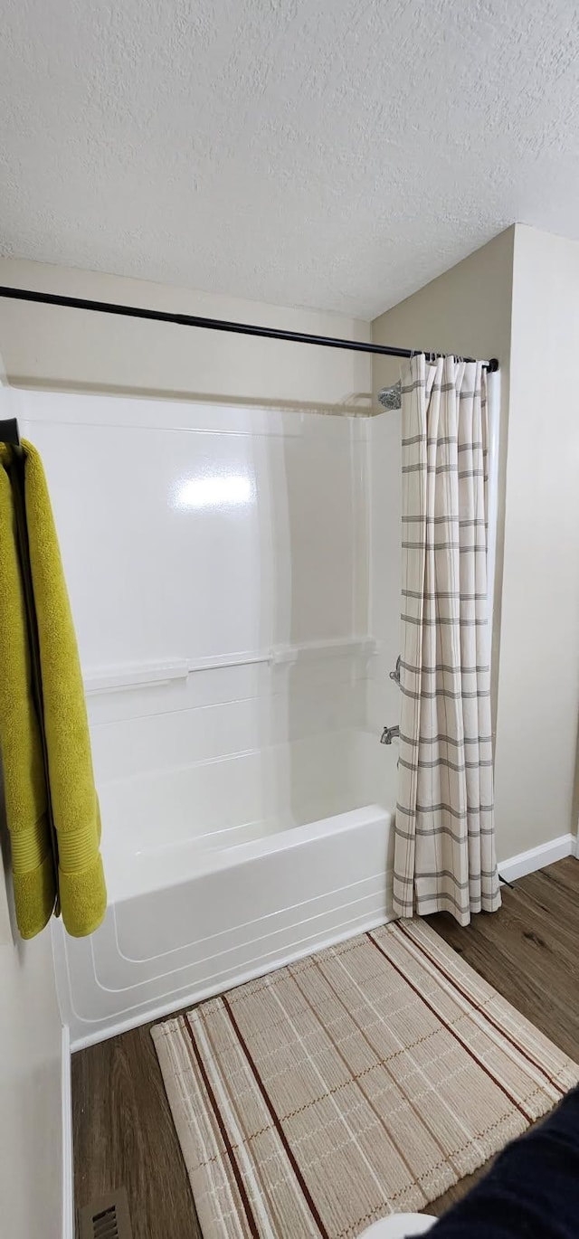 bathroom with a textured ceiling, baseboards, wood finished floors, and shower / tub combo with curtain