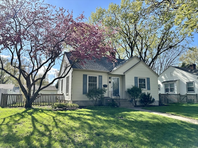 bungalow featuring central AC unit, a shingled roof, fence, and a front yard