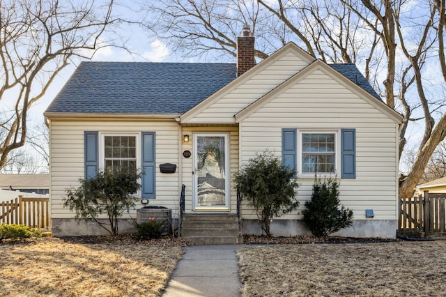 bungalow-style house featuring entry steps, roof with shingles, a chimney, and fence