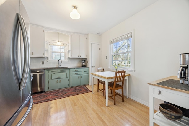 kitchen with a sink, white cabinets, appliances with stainless steel finishes, light wood-type flooring, and backsplash