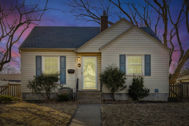 view of front of house featuring entry steps, central AC, fence, roof with shingles, and a chimney