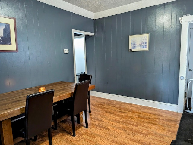 dining space featuring light wood-type flooring, baseboards, and a textured ceiling