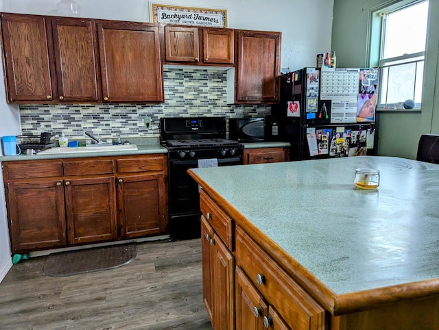 kitchen featuring wood finished floors, a sink, light countertops, black appliances, and tasteful backsplash