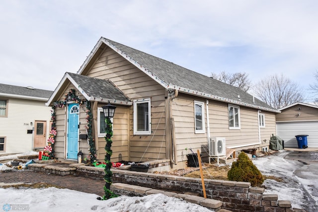 back of property with ac unit, a shingled roof, a detached garage, and an outbuilding