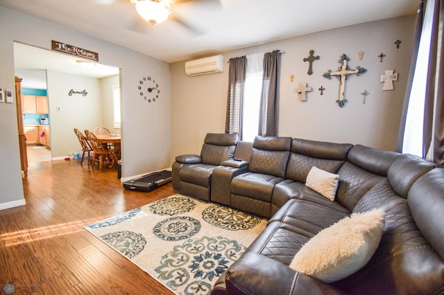 living room with a wall unit AC, ceiling fan, baseboards, and wood finished floors