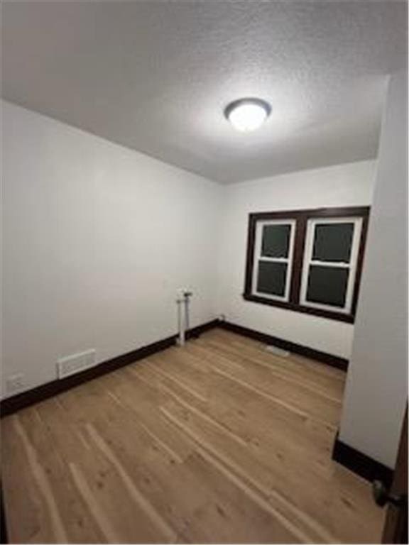 empty room with a textured ceiling, baseboards, and wood finished floors