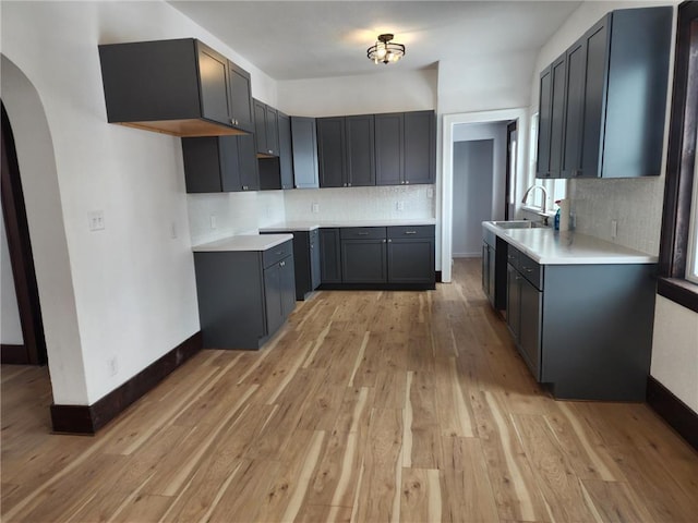 kitchen with arched walkways, a sink, baseboards, light wood-type flooring, and tasteful backsplash