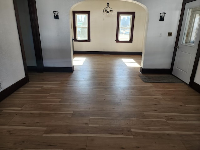 unfurnished dining area featuring baseboards, arched walkways, and wood finished floors