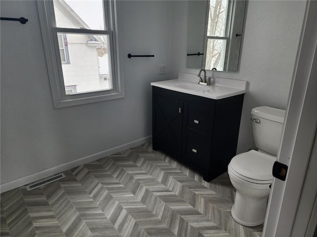 bathroom with toilet, vanity, visible vents, and a healthy amount of sunlight