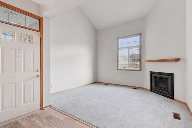 foyer featuring lofted ceiling, a glass covered fireplace, visible vents, and baseboards