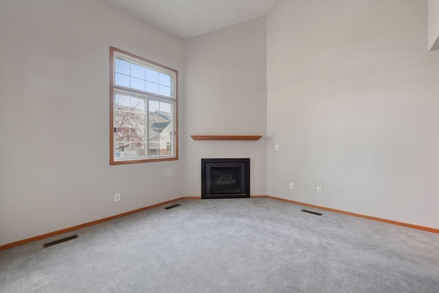 unfurnished living room featuring carpet floors, a glass covered fireplace, visible vents, and baseboards