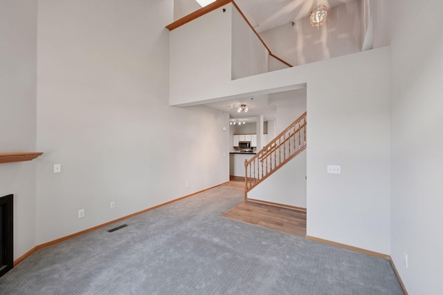 unfurnished living room featuring carpet floors, visible vents, a towering ceiling, stairway, and a tiled fireplace