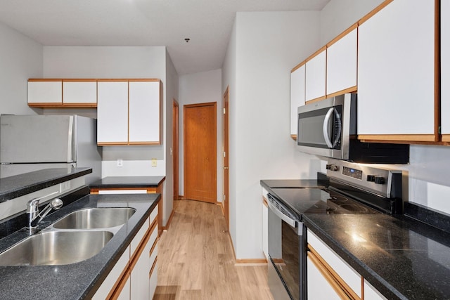 kitchen featuring light wood-style flooring, stainless steel appliances, a sink, white cabinetry, and baseboards