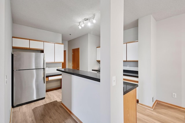 kitchen with light wood-style flooring, white cabinetry, a textured ceiling, and freestanding refrigerator