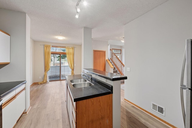 kitchen featuring visible vents, dark countertops, light wood-style flooring, a kitchen island with sink, and a sink