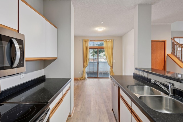 kitchen with stainless steel appliances, a sink, white cabinetry, light wood-type flooring, and dark countertops