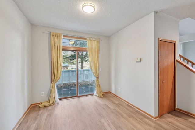 empty room with light wood-type flooring, a textured ceiling, baseboards, and stairs