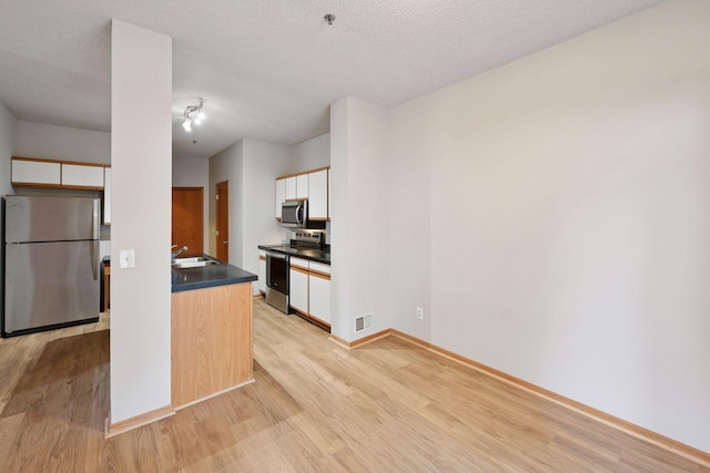 kitchen with dark countertops, light wood-style flooring, appliances with stainless steel finishes, white cabinetry, and a sink