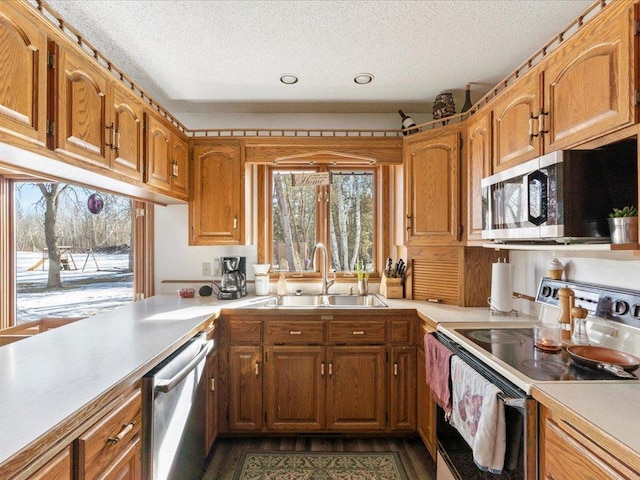 kitchen with brown cabinets, stainless steel appliances, light countertops, and a sink