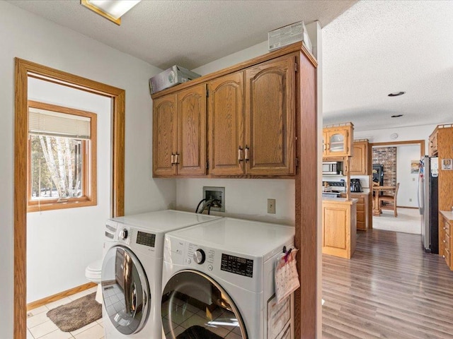 clothes washing area with baseboards, light wood finished floors, cabinet space, a textured ceiling, and washing machine and dryer