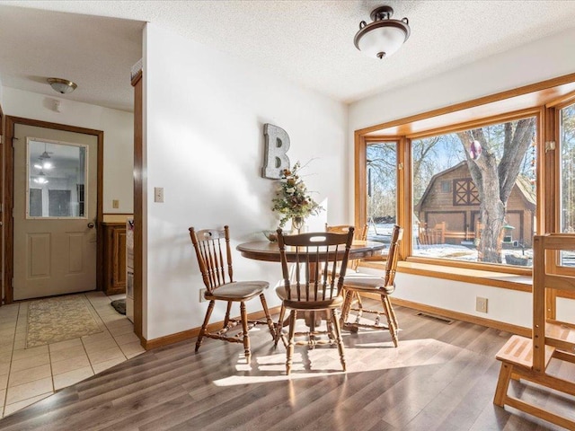dining space featuring visible vents, a textured ceiling, light wood-type flooring, and baseboards