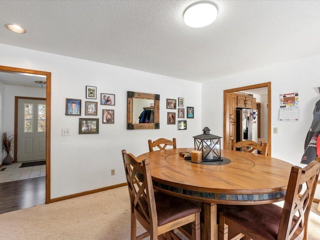 dining room with baseboards, a textured ceiling, and light carpet