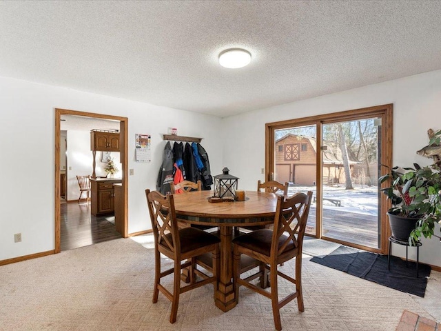 dining room with light colored carpet, a textured ceiling, and baseboards