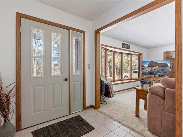 foyer entrance with a textured ceiling, light tile patterned flooring, baseboards, and light carpet