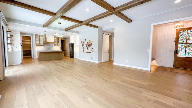 unfurnished living room featuring a barn door, coffered ceiling, baseboards, light wood-type flooring, and beam ceiling