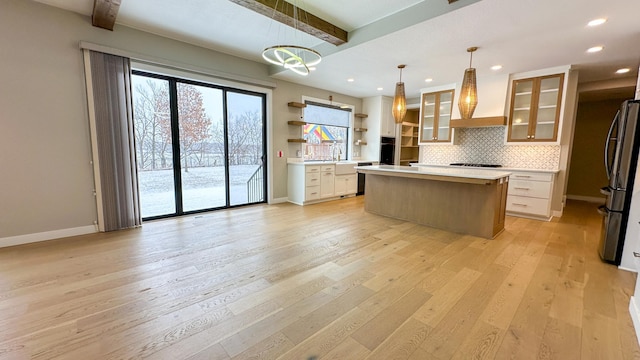 kitchen featuring tasteful backsplash, freestanding refrigerator, light countertops, wall chimney range hood, and beam ceiling