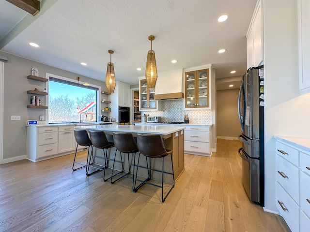 kitchen featuring oven, premium range hood, a kitchen breakfast bar, freestanding refrigerator, and open shelves