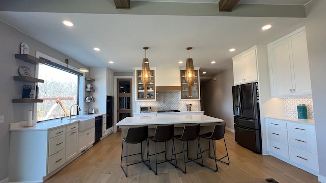 kitchen with black appliances, custom exhaust hood, a center island, open shelves, and a kitchen bar