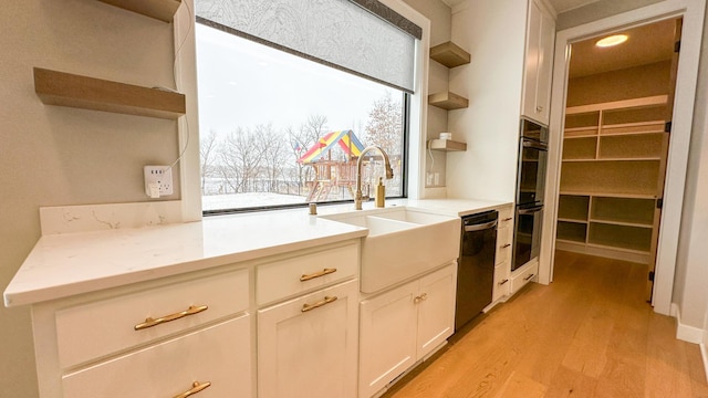 kitchen with light wood finished floors, open shelves, white cabinetry, a sink, and black appliances