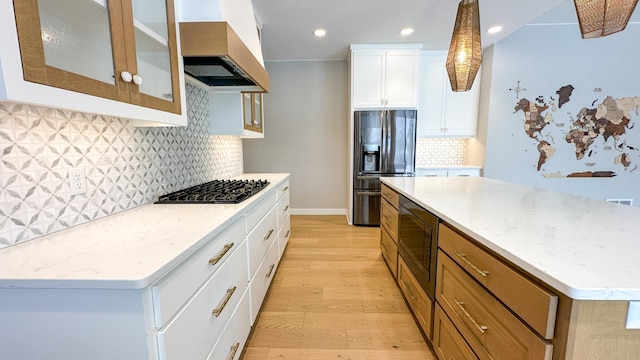 kitchen with light wood-style floors, built in microwave, black refrigerator with ice dispenser, wall chimney range hood, and gas cooktop