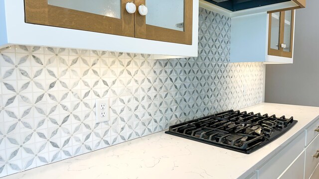 kitchen featuring black gas cooktop, light stone countertops, glass insert cabinets, and decorative backsplash