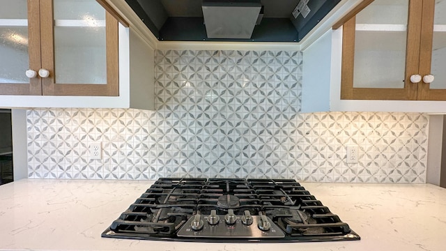 kitchen with glass insert cabinets, backsplash, black gas stovetop, and light stone countertops