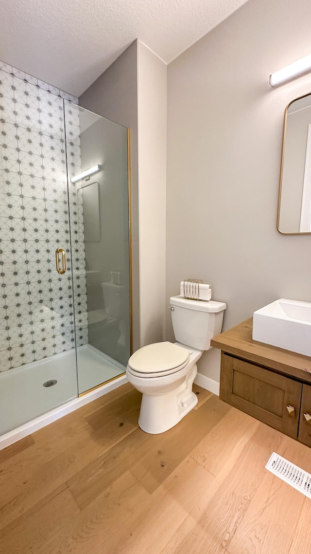 full bathroom featuring a stall shower, a textured ceiling, toilet, and wood finished floors