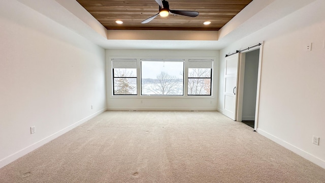 empty room featuring wood ceiling, a raised ceiling, baseboards, and a barn door