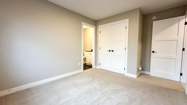 unfurnished bedroom featuring a closet, carpet, ensuite bath, and baseboards