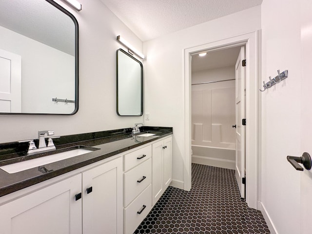 bathroom with double vanity, a textured ceiling, baseboards, and a sink