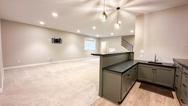 kitchen with dark countertops, light carpet, a sink, a peninsula, and baseboards