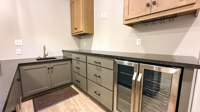 kitchen featuring dark countertops, beverage cooler, light wood-style flooring, and a sink