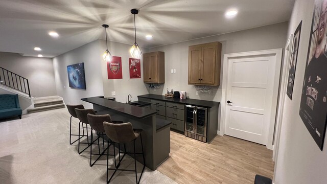 kitchen featuring dark countertops, wine cooler, a breakfast bar area, light wood-type flooring, and a sink